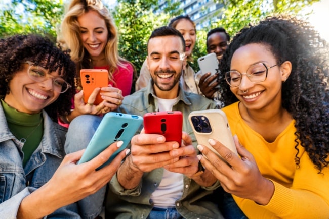 A group of young friends are watching their smartphones and smiling.